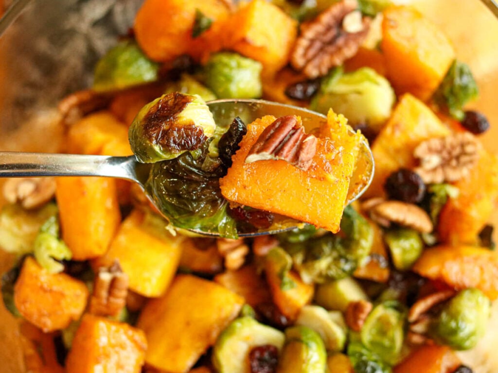 A spoon scooping roasted Brussels sprouts and butternut squash out of a bowl.