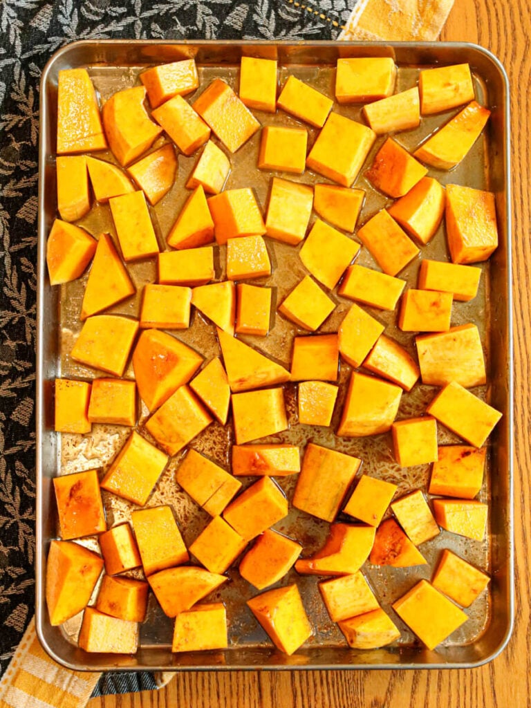 Butternut squash cubes on a sheet pan on a table.