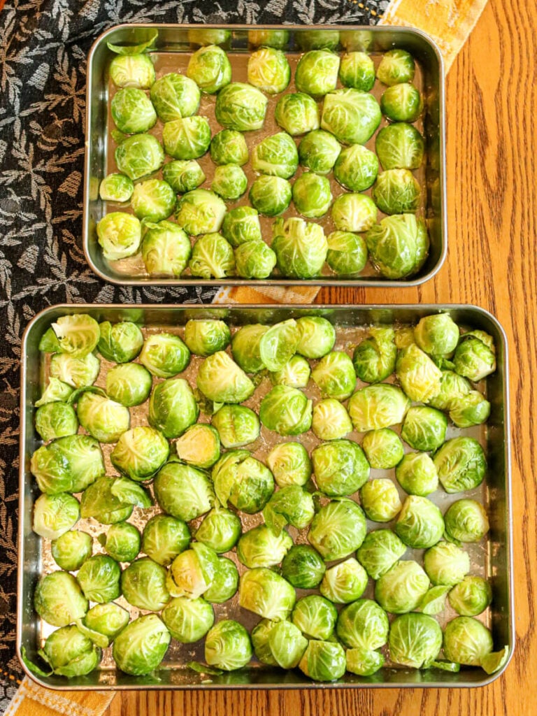 Brussels sprout halves on two sheet pans on a wood surface.