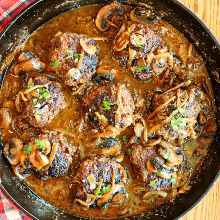 Close up view of Salisbury steak patties in a cast iron skillet.