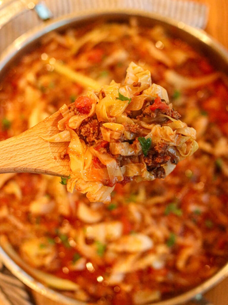 Cabbage bowls being scooped out of a saute pan with a wooden spoon.