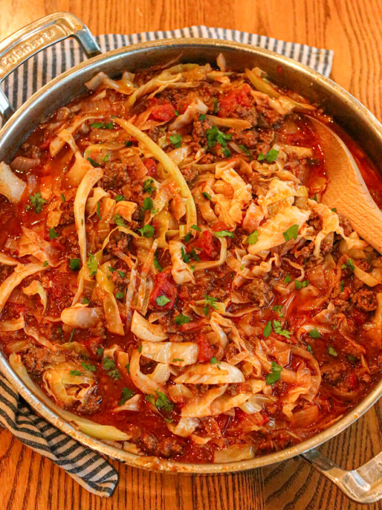 Cabbage bowls in a saute pan with a wooden serving spoon on a wooden table.