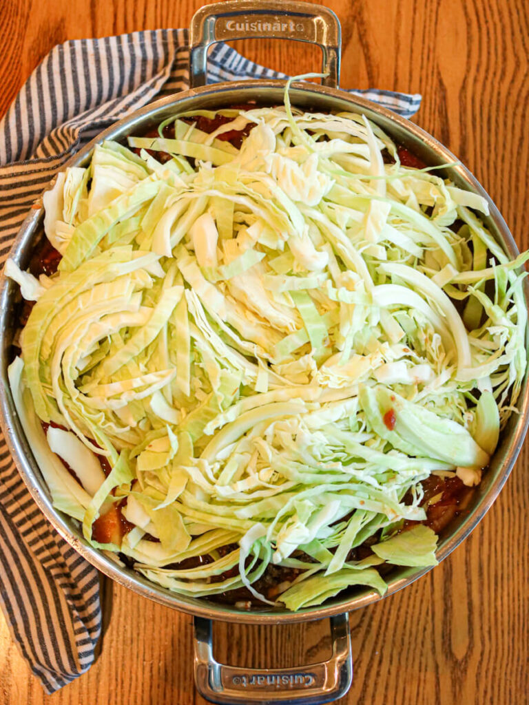 Shredded cabbage over ground beef and tomato sauce in a sauté pan.