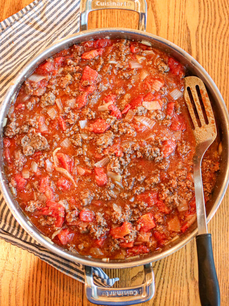 Ground beef with tomato sauce in a sauté pan on a wooden table.