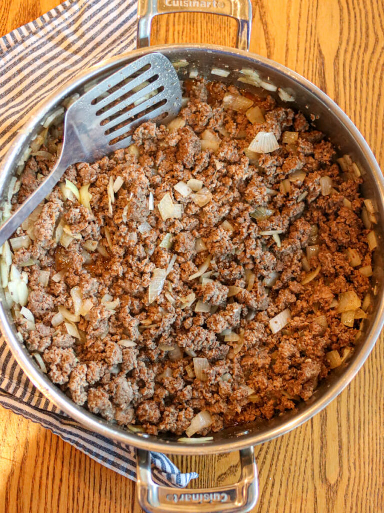 Ground beef and diced onions browning in saute pan with a wooden background.