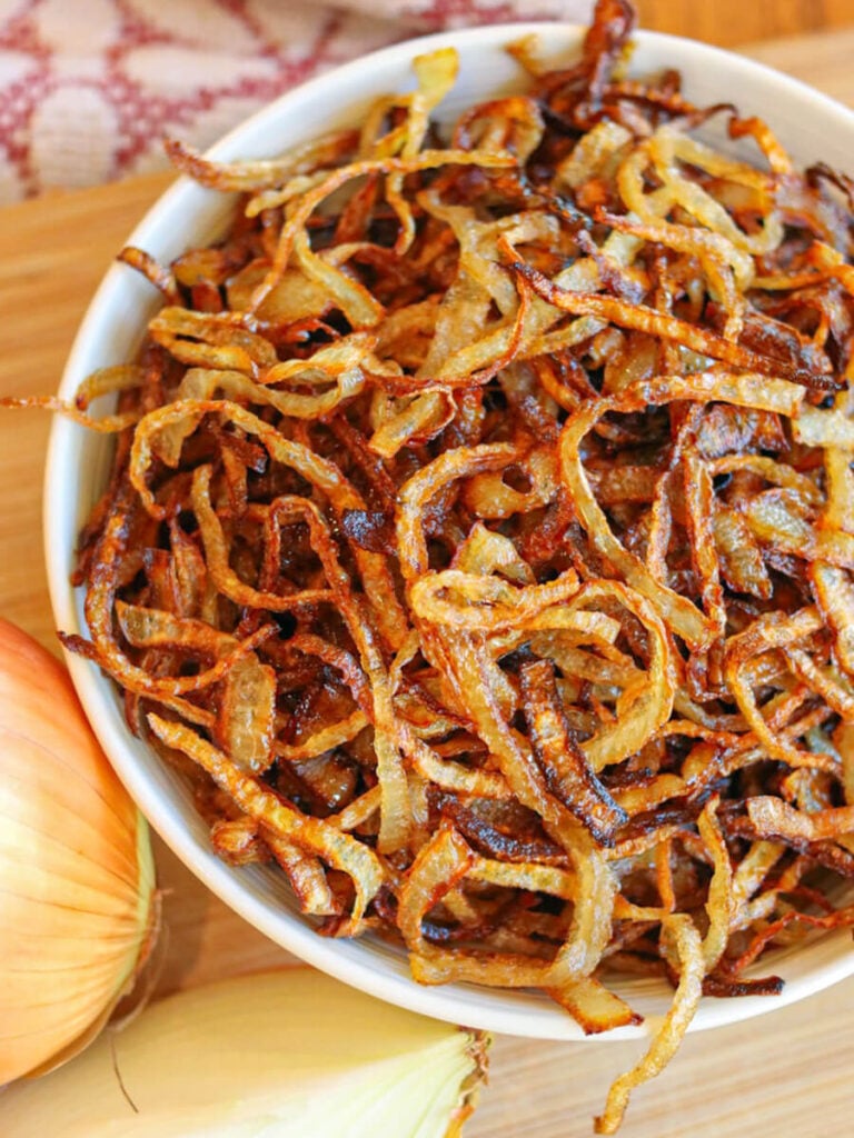 A bowl of gluten-free fried onions in a white bowl on a wooden cutting board.