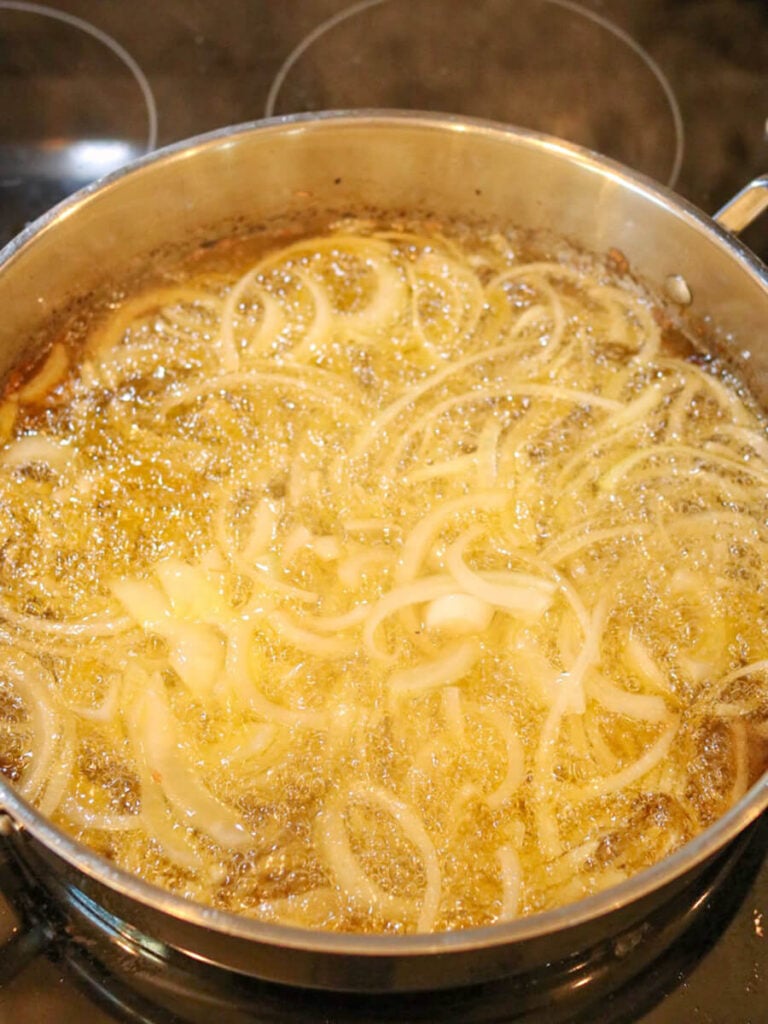 Onion slices frying in avocado oil on the stove.