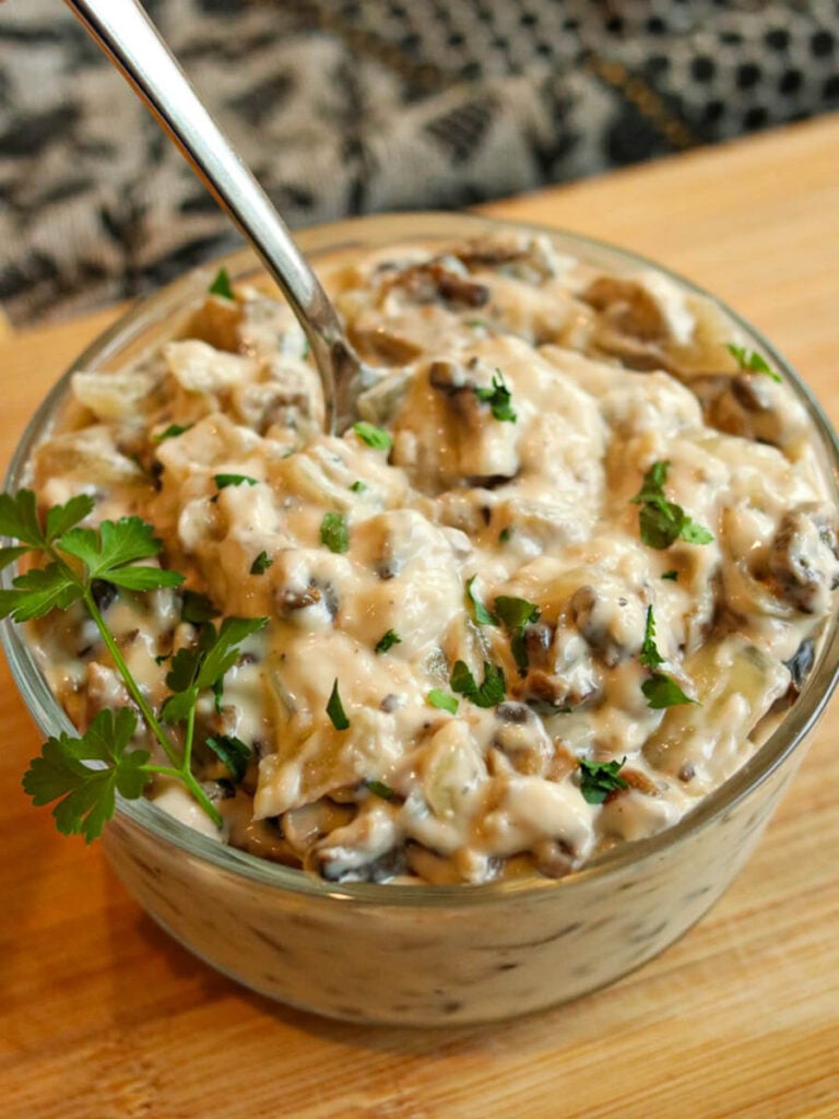 Gluten-free cream of mushroom soup garnished with fresh parsley in a glass bowl with a spoon in it on a wooden surface.