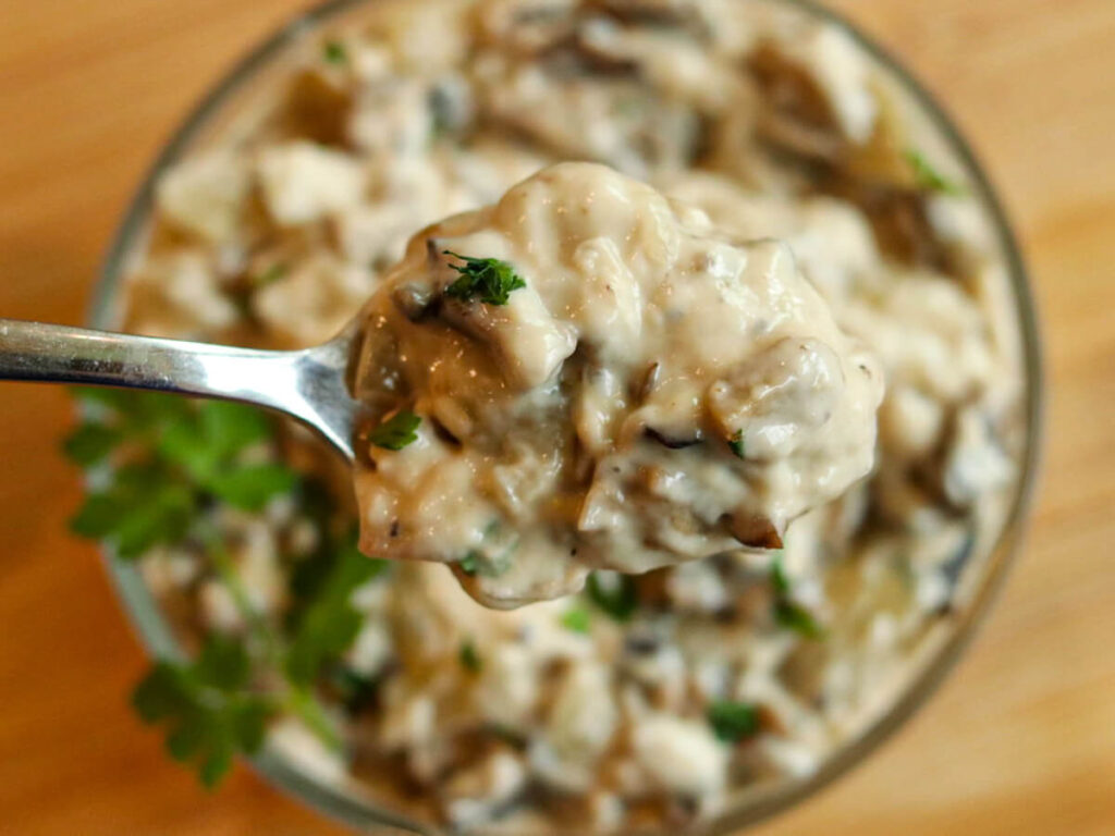 A scoop of homemade cream of mushroom soup on a spoon with a bowl of soup in the background.