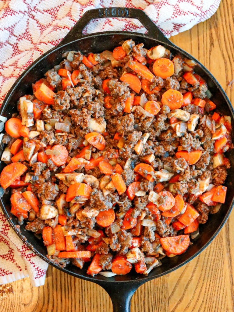 Meat, carrots, and other vegetables cooking in a skillet.