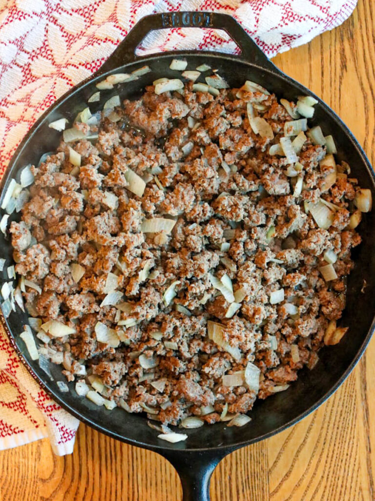 Ground beef and diced onions browning in a cast iron skillet with a wooden background.