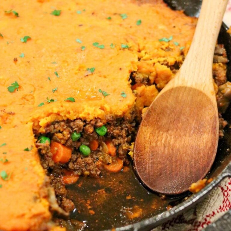 Closeup view of a wooden spoon in a cast iron skillet with sweet potato cottage pie with a piece taken out.