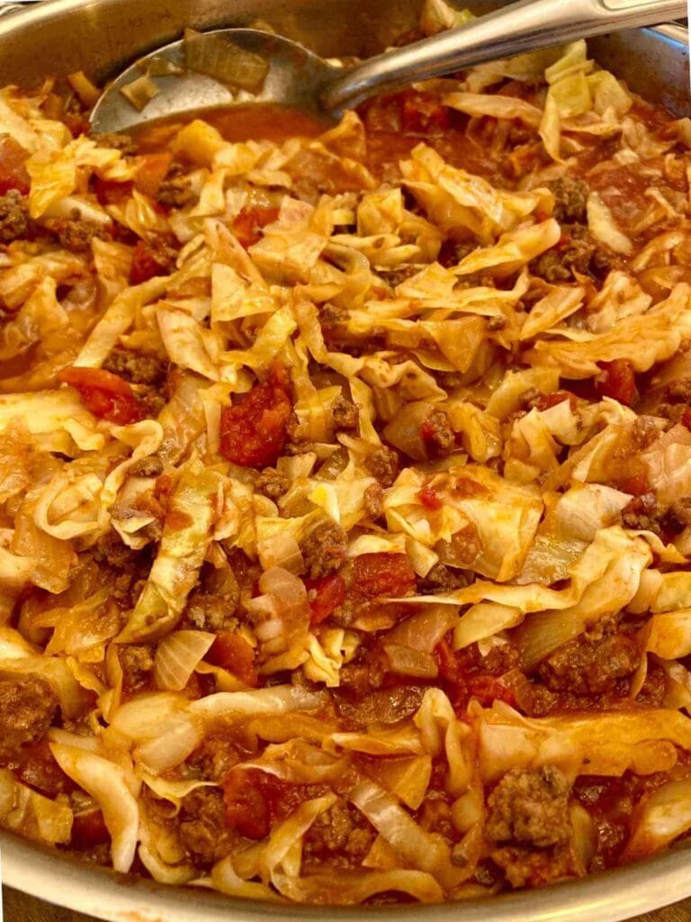 Closeup of spoon in skillet with cabbage roll in a bowl