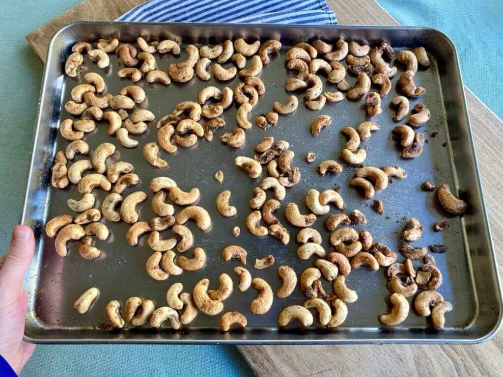 Hand holding baking sheet with roasted cashews