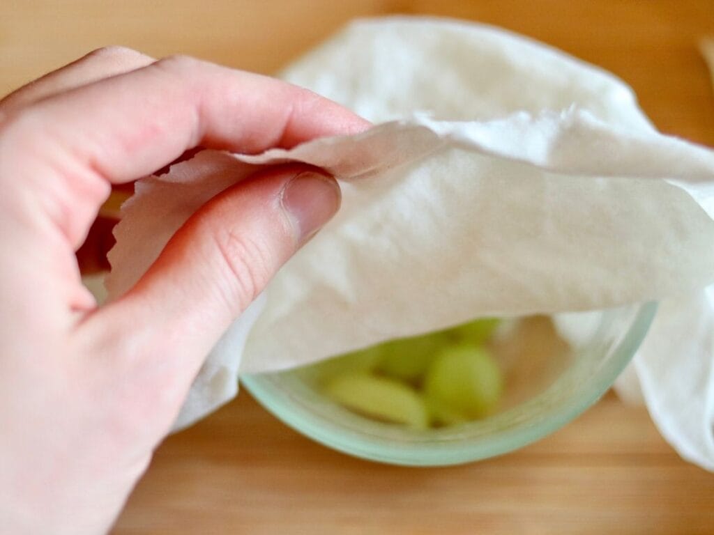 Hand covering bowl of grapes with beeswax food wrap.