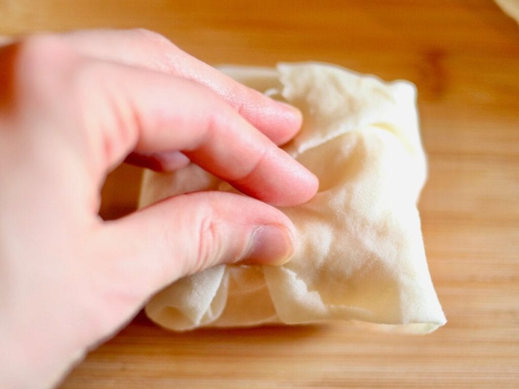 Hand folding beeswax food wrap around block of cheese.