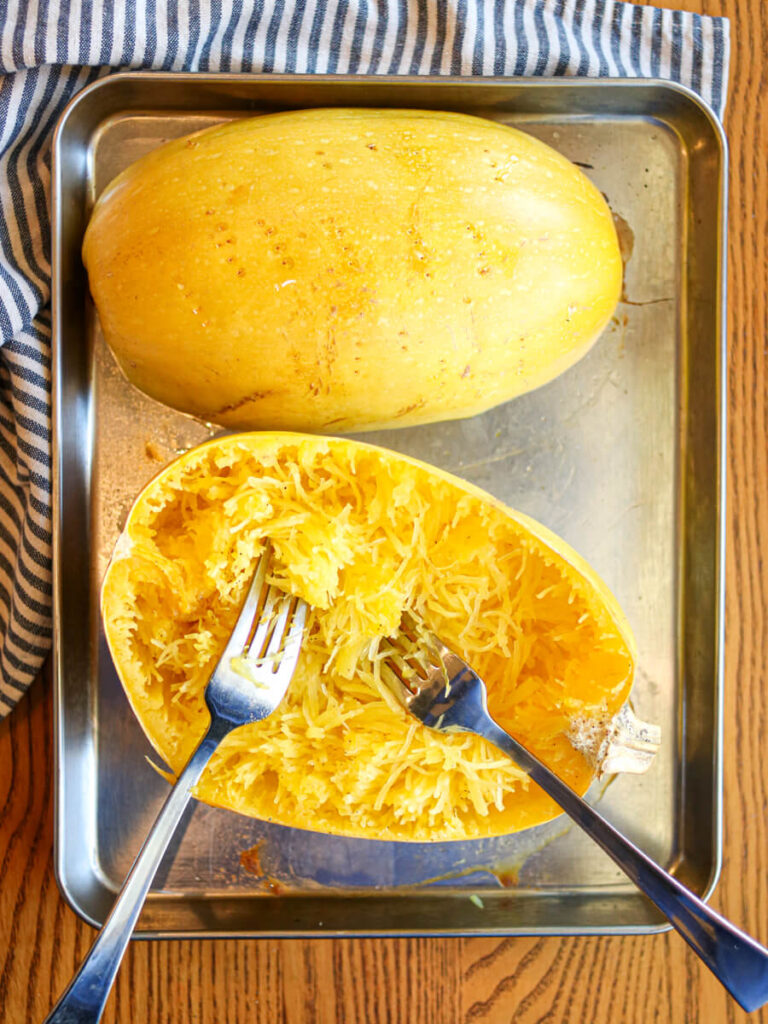 Shredding a cooked spaghetti squash with forks.