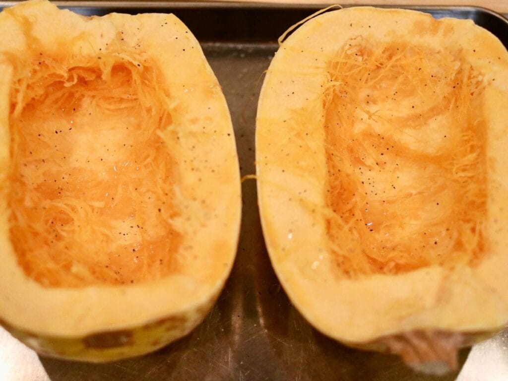 Two spaghetti squash halves with seeds removed and oil, salt, and pepper on them.