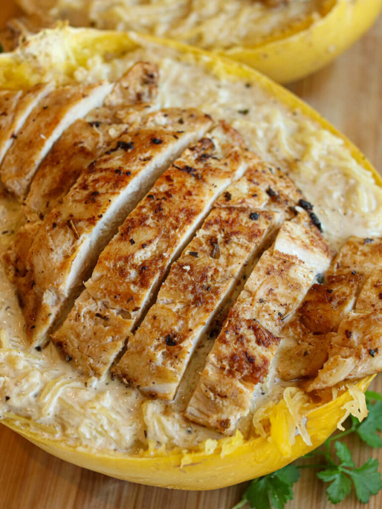Closeup of chicken Alfredo spaghetti squash in a squash shell on a wood surface.