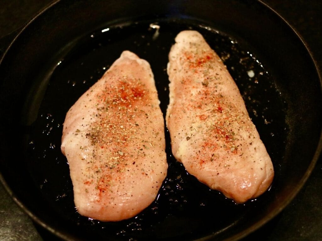 2 chicken breasts cooking in cast iron skillet