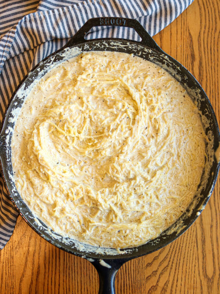 Adding spaghetti squash to parmesan sauce in a cast iron skillet.