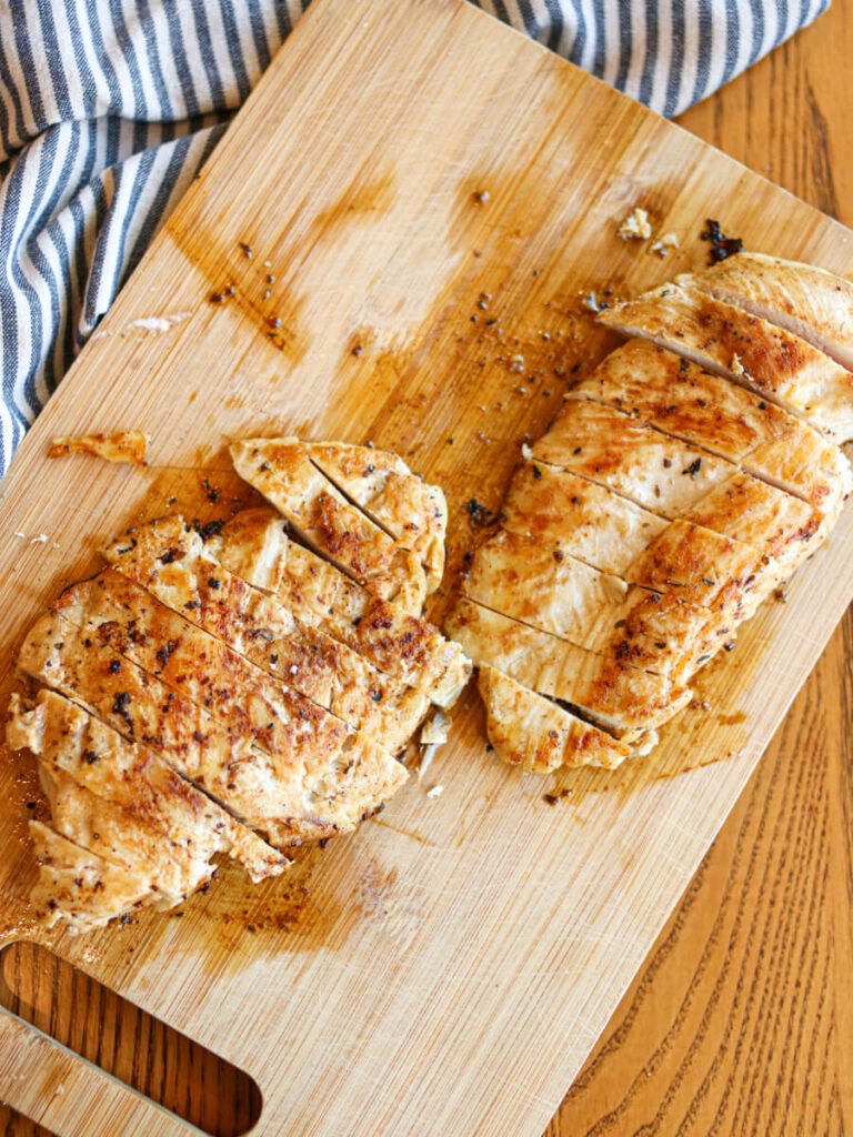 Two sliced chicken breasts on a wood cutting board.