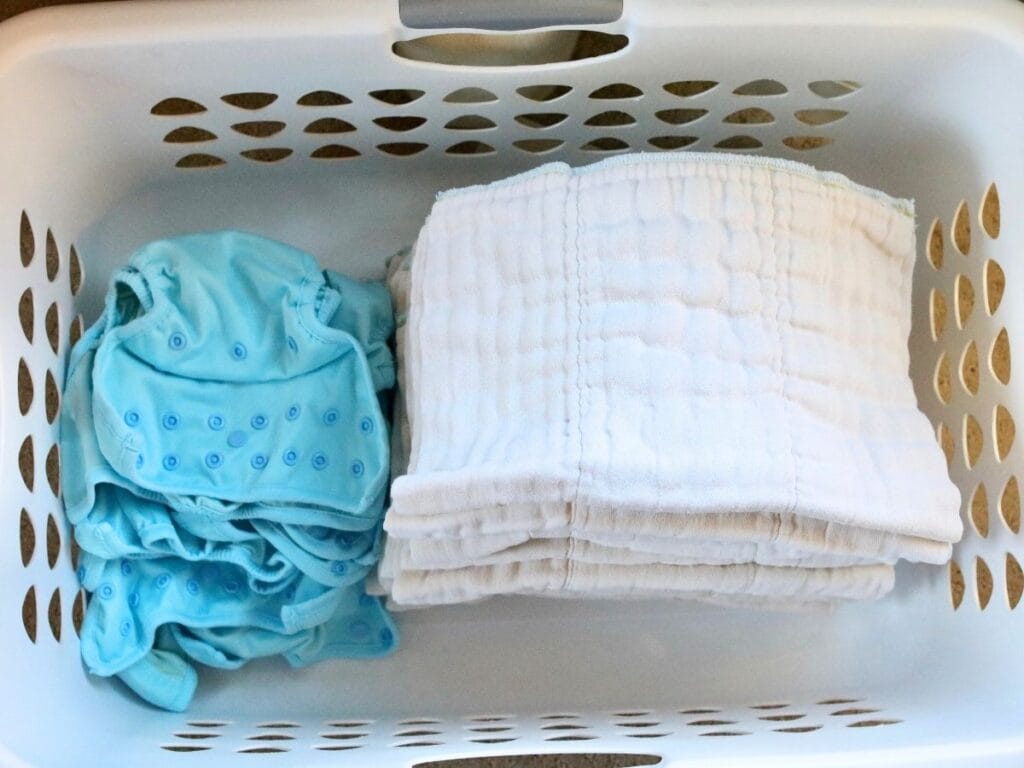 Cloth diaper inserts and covers neatly folded in a laundry basket.