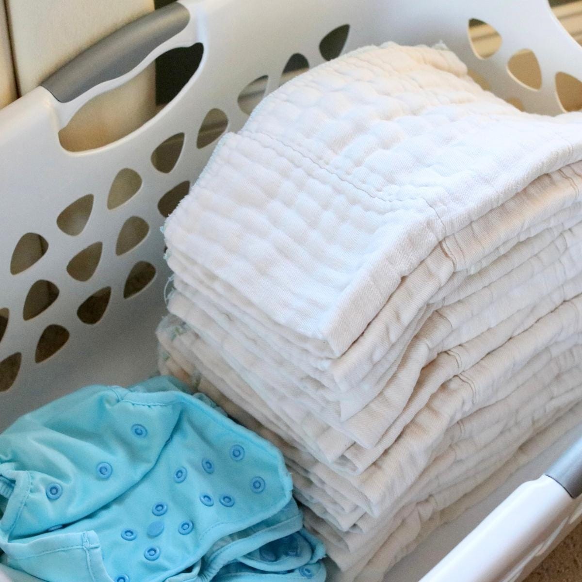 Cloth diaper inserts and covers in a laundry basket.
