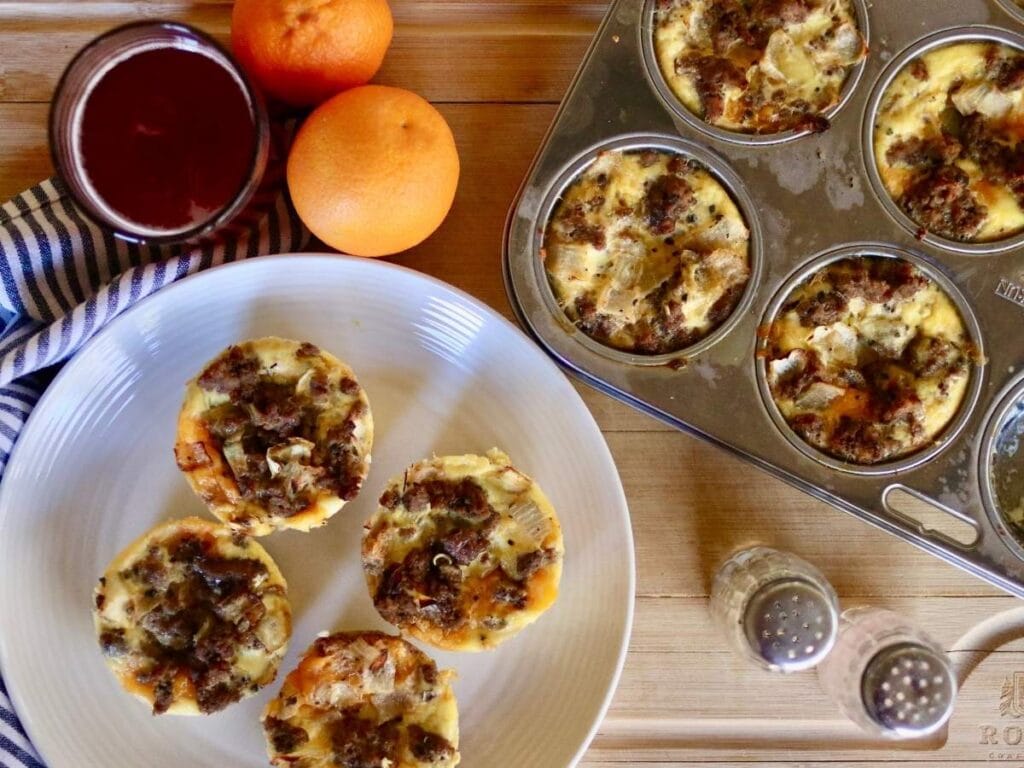 4 high protein egg bites on a plate and in muffin tin with juice and oranges