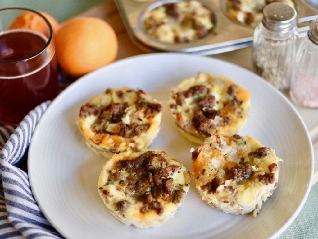 4 high protein egg bites on a plate and in muffin tin in the background with juice and oranges