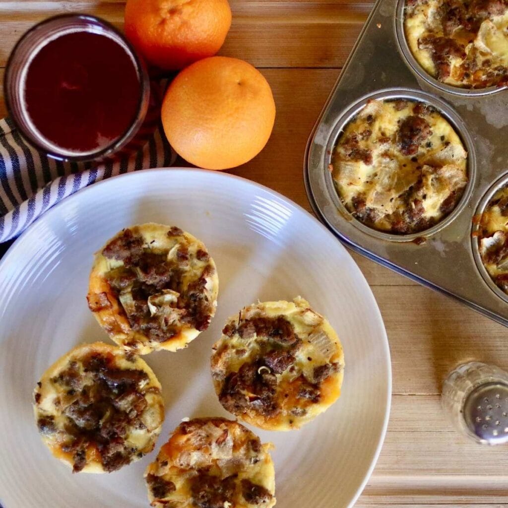 High protein egg bites on a plate and in muffin tin with juice and oranges