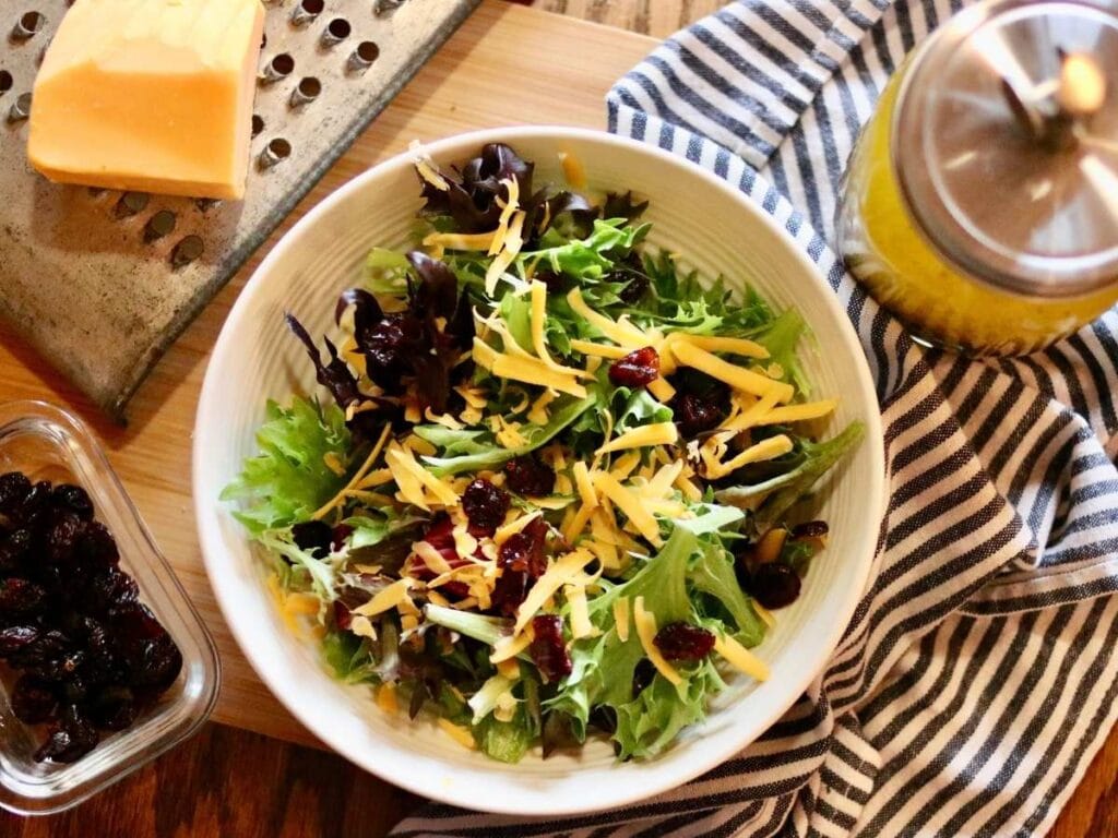 Salad with Italian vinaigrette, dried cranberries, and a block of cheese on a grater in the background
