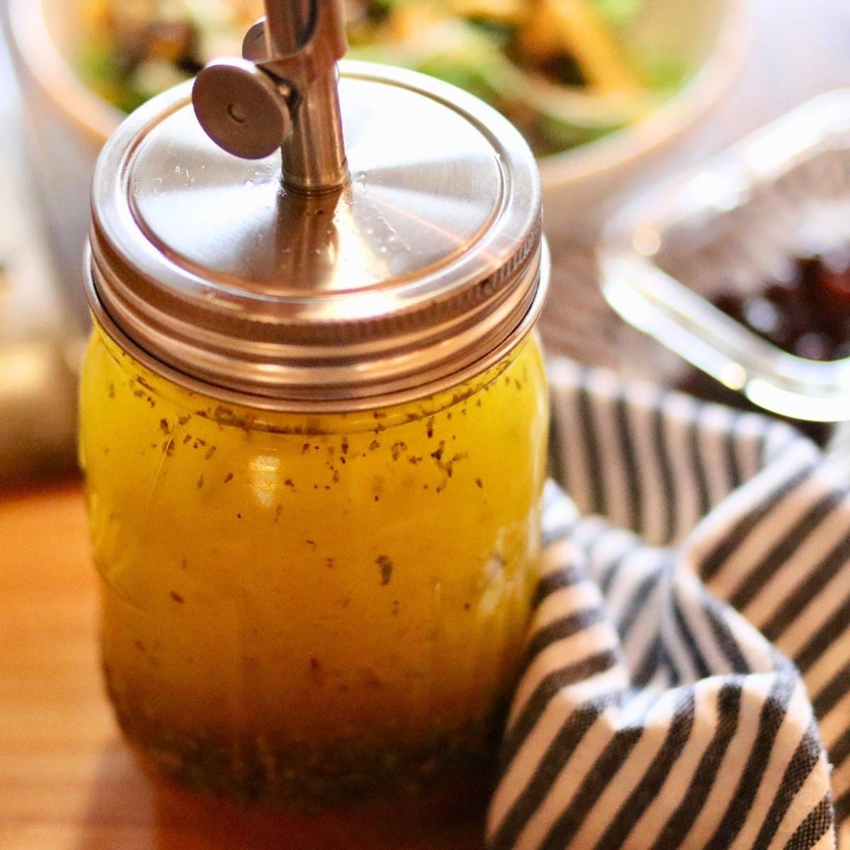 Jar of Italian vinaigrette with pour spout with a salad in the background