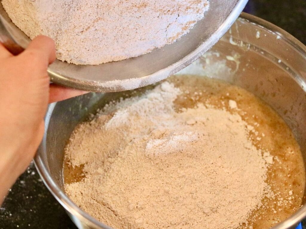 Dumping dry ingredients into a bowl of wet ingredients.