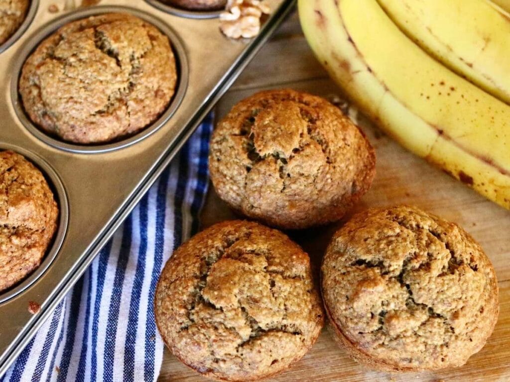 3 oat flour banana muffins beside muffin pan with muffins and banana.