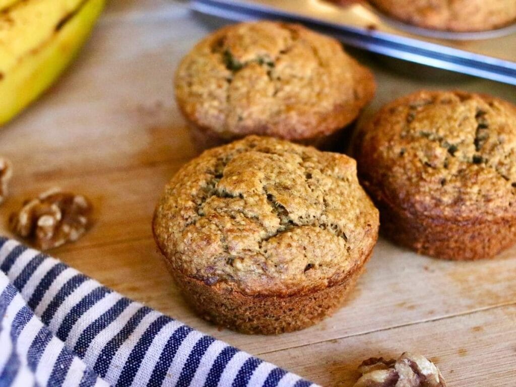 3 oat flour banana muffins with a cloth napkin and walnuts.