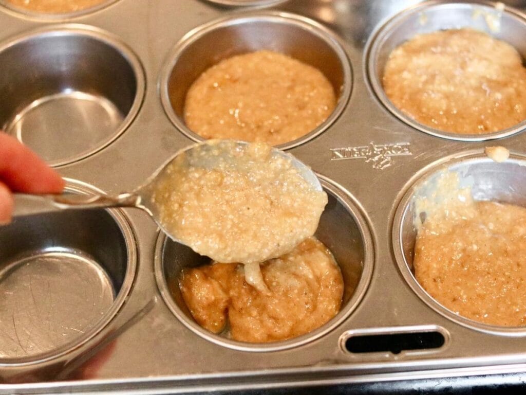 Scooping batter into a stainless steel muffin pan.
