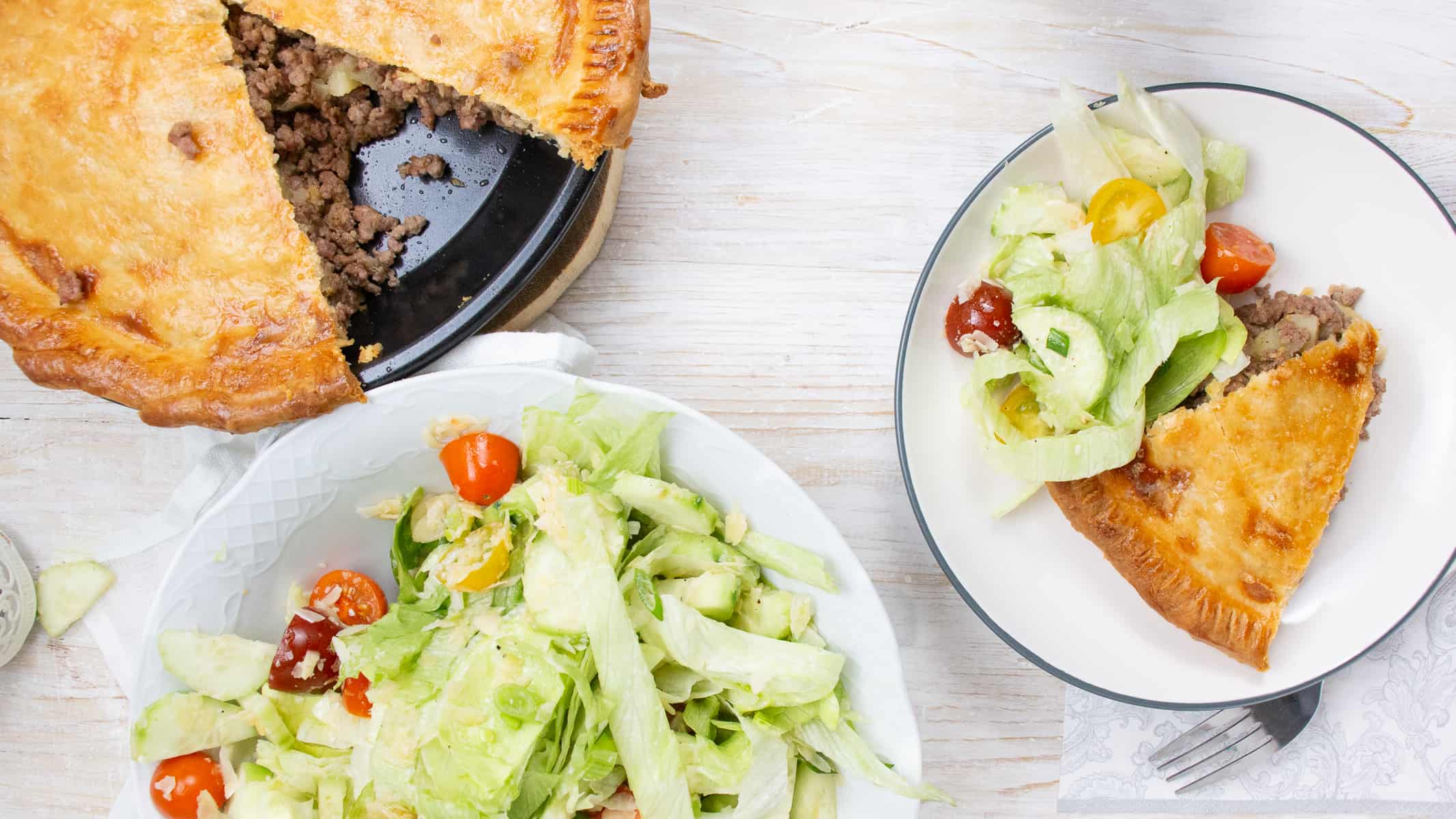 tourtiere in a pie pan and slice on a plate with salad