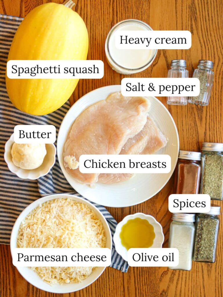 Labeled ingredients on a wooden table including spaghetti squash, chicken, cream, butter, parmesan, oil, and spices.