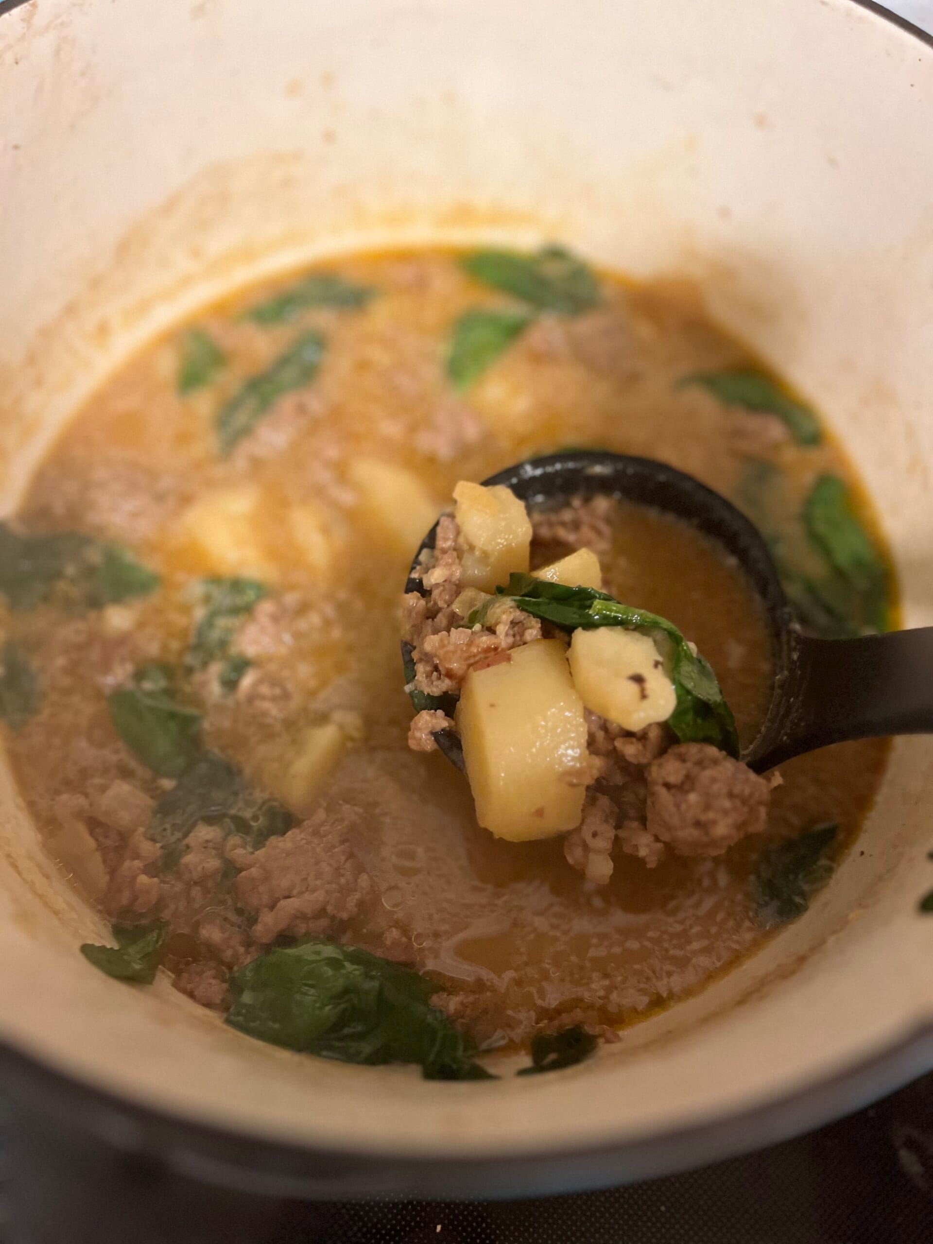 Spoon scooping sausage and potato soup out of bowl
