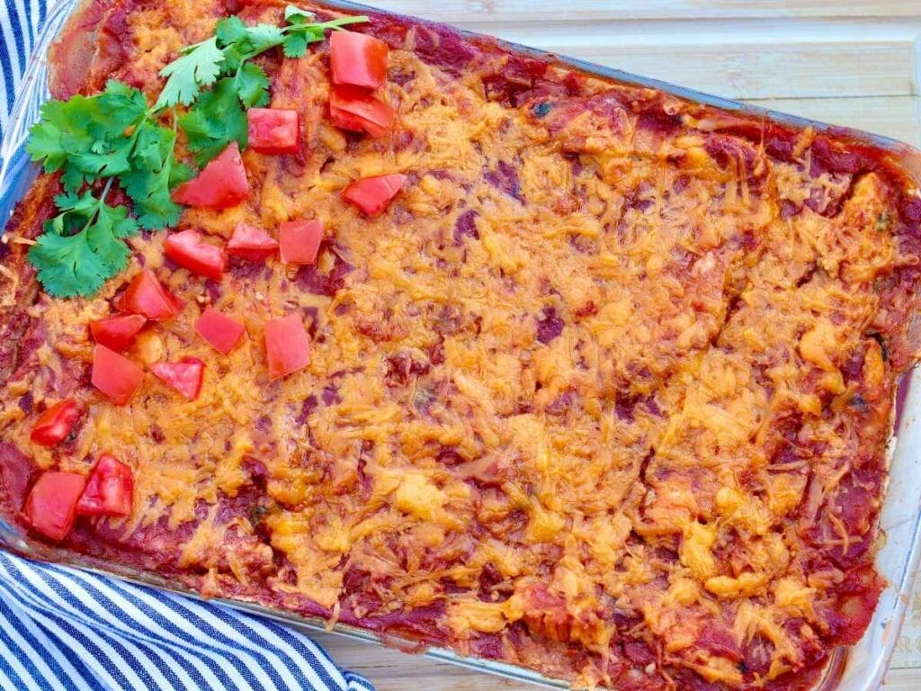 Chicken enchilada casserole in a baking dish with chopped tomatoes and fresh cilantro on top.