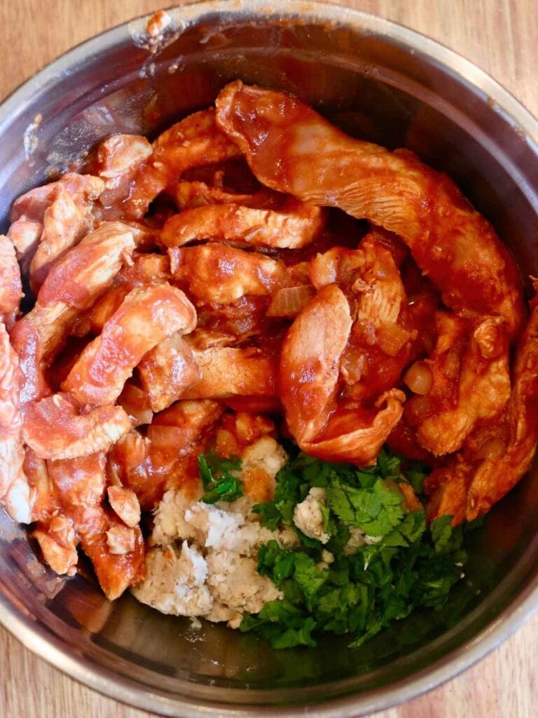 Chicken slices, cilantro, and refried beans in a mixing bowl.