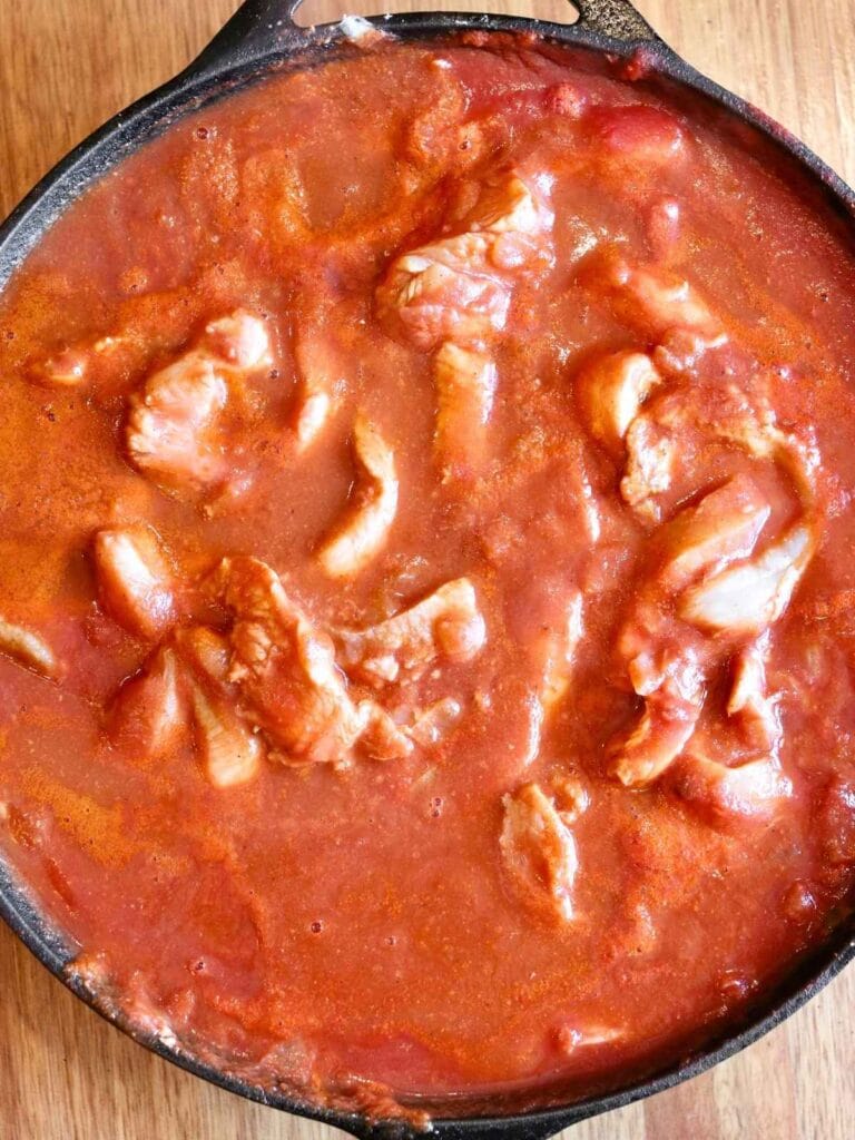 Chicken slices simmering in tomato sauce.