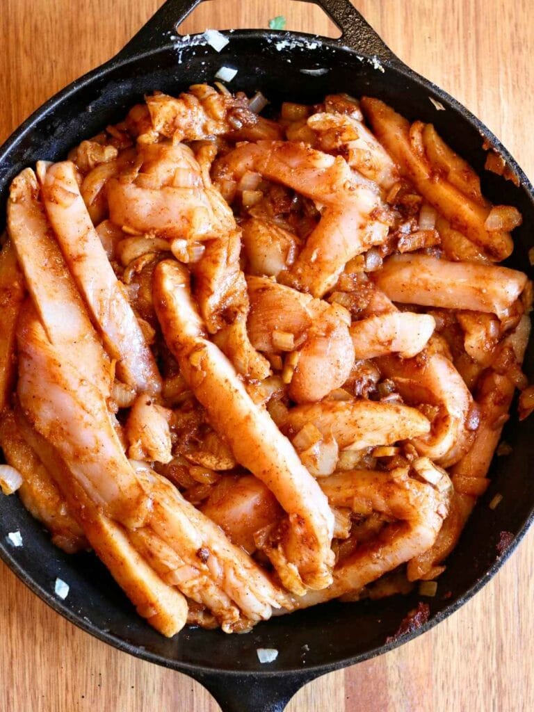 Adding chicken slices to spices and onions in a skillet.