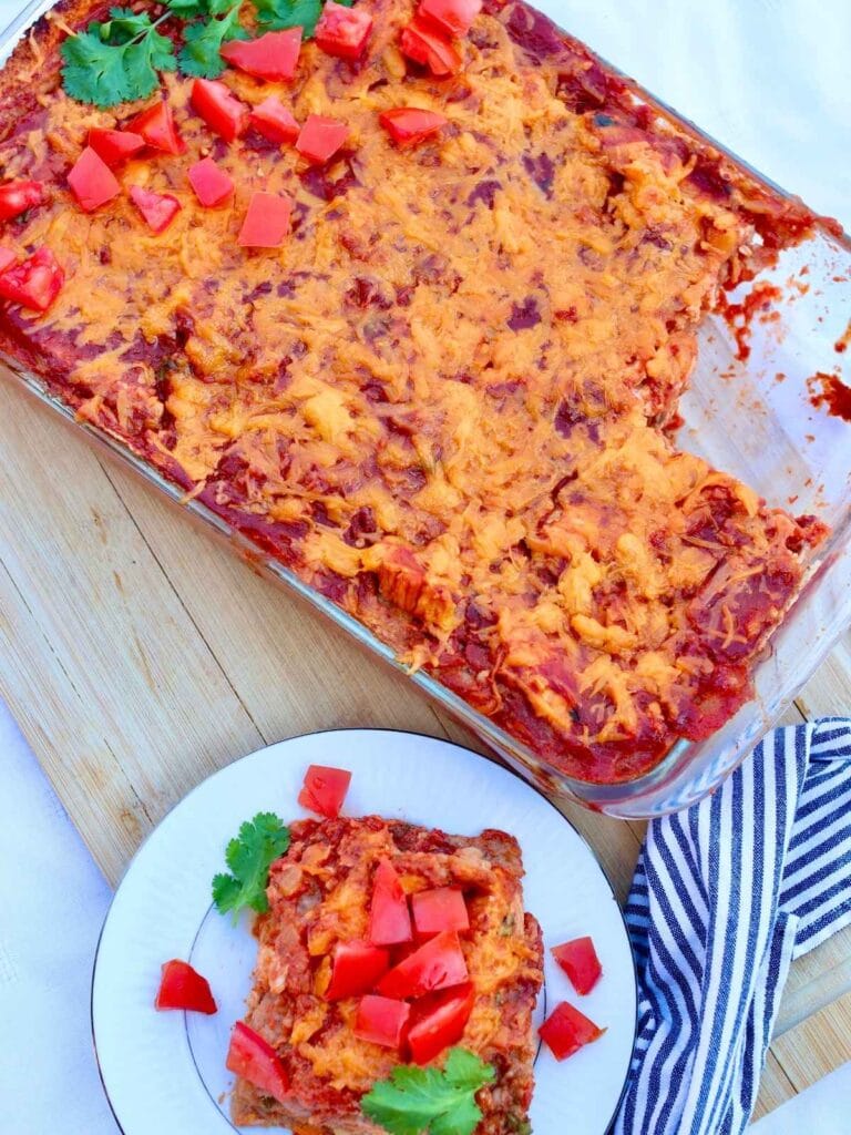 Chicken enchilada casserole in a baking dish with a slice on a plate.