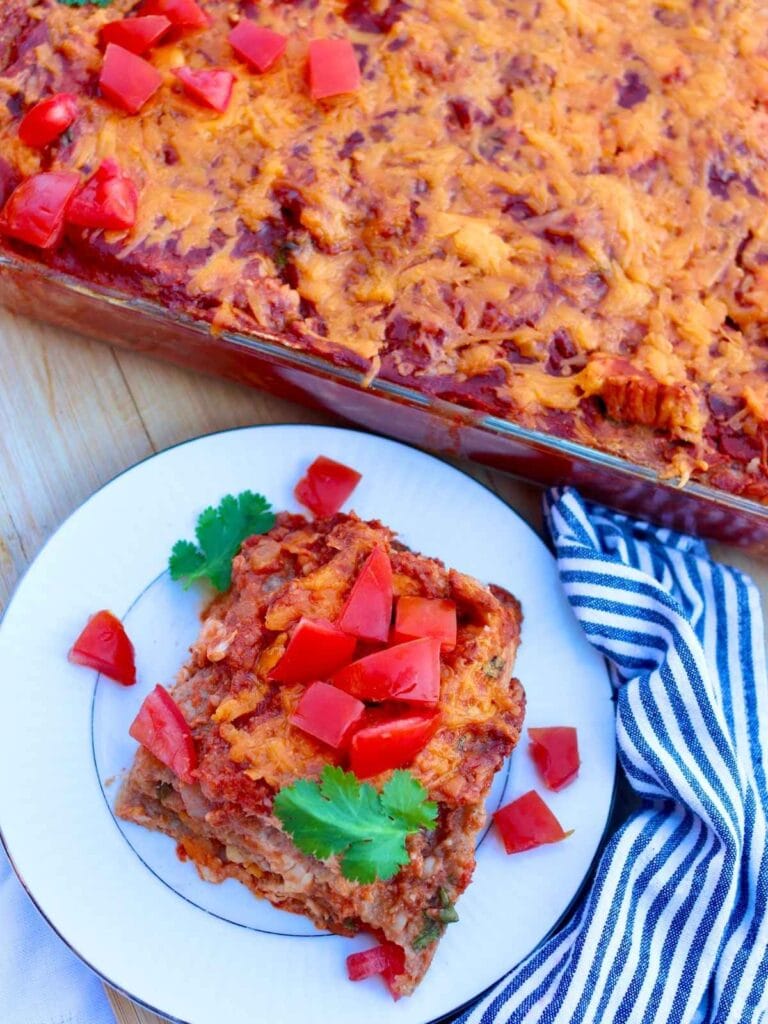 Chicken enchilada casserole in a pan and a slice on a plate with chopped tomatoes.