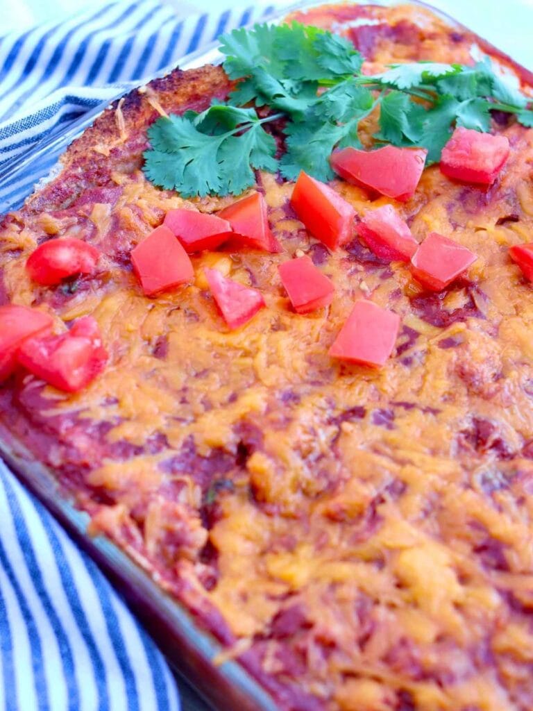 Chicken enchilada casserole in a baking dish garnished with chopped tomatoes and fresh cilantro.