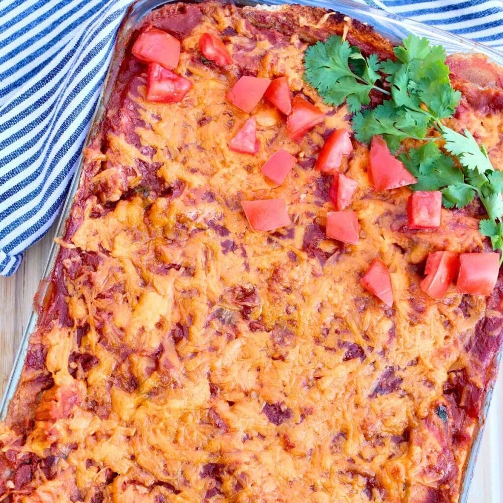 Closeup of chicken enchilada casserole in a baking dish garnished with chopped tomatoes and fresh cilantro.
