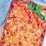 Closeup of chicken enchilada casserole in a baking dish garnished with chopped tomatoes and fresh cilantro.