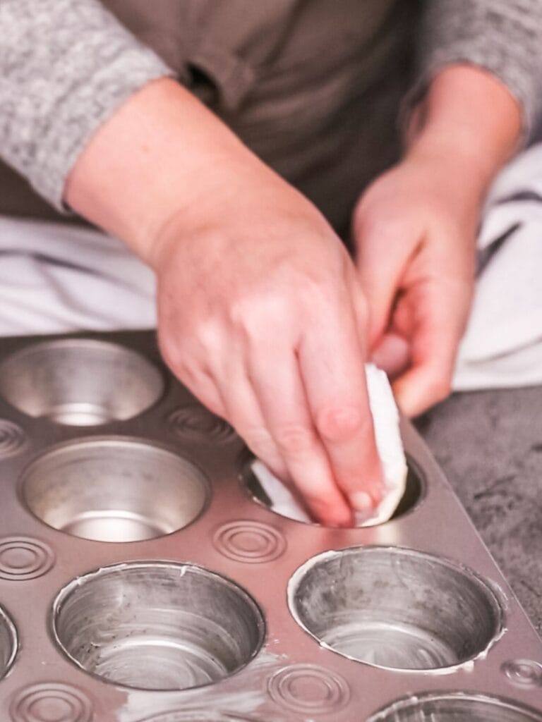 Greasing a muffin pan with butter.